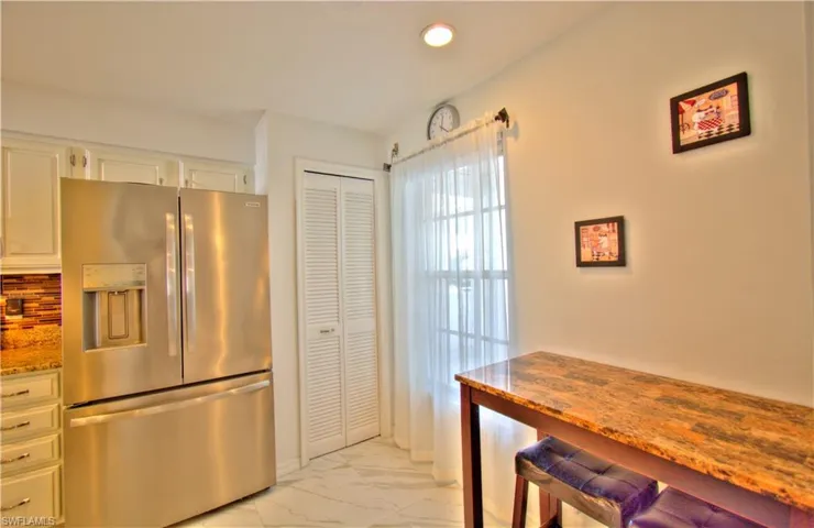 Kitchen with stainless steel refrigerator with ice dispenser, light stone counters, light marble finish flooring, white cabinetry, and recessed lighting