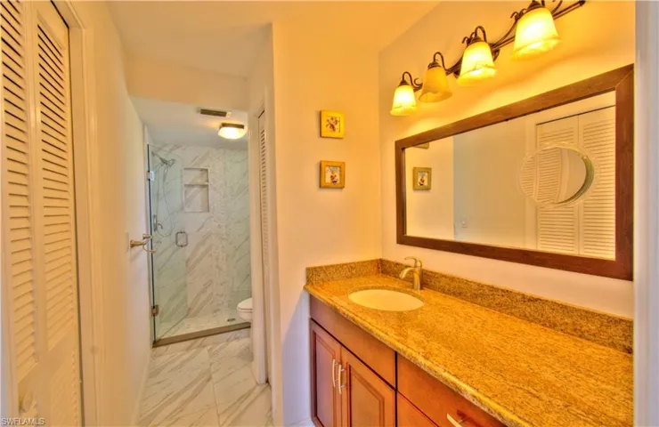 Bathroom with a closet, vanity, a marble finish shower, and light marble finish floors
