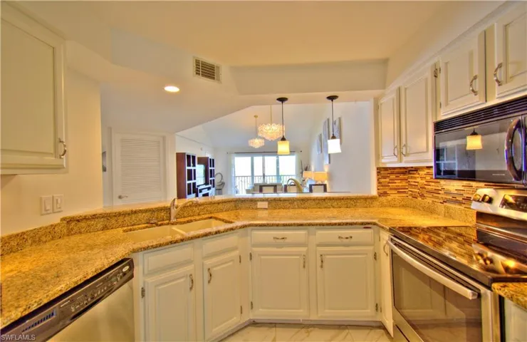 Kitchen featuring stainless steel appliances, a chandelier, a peninsula, white cabinetry, and vaulted ceiling