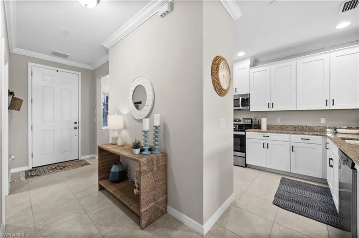 Kitchen with crown molding, light stone countertops, appliances with stainless steel finishes, light tile patterned flooring, and white cabinetry