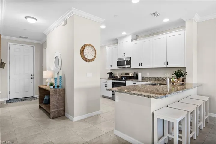 Kitchen with white cabinets, appliances with stainless steel finishes, ornamental molding, and dark stone counters
