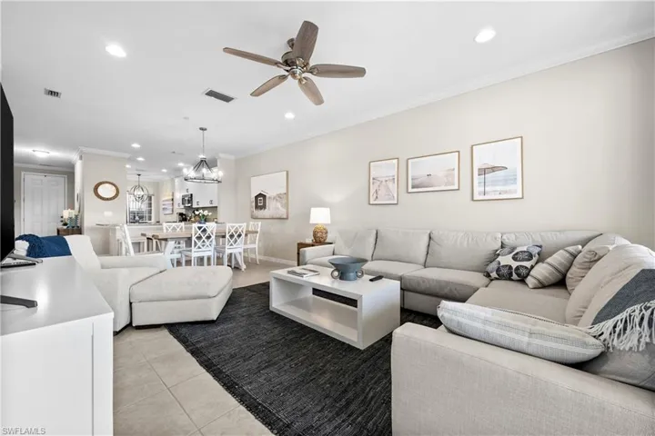 Tiled living room with ceiling fan with notable chandelier and ornamental molding