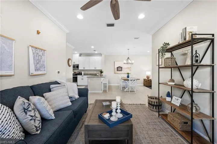 Tiled living room featuring crown molding and ceiling fan with notable chandelier