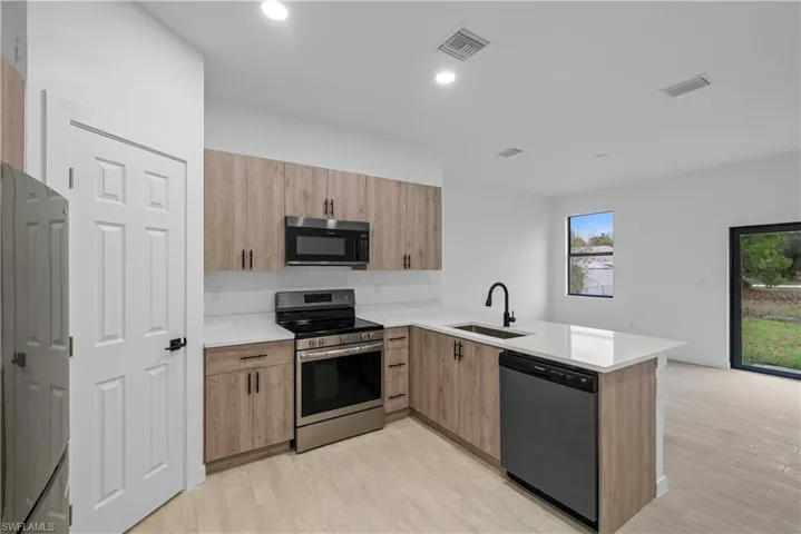 Kitchen with stainless steel appliances, a peninsula, light stone counters, light wood-type flooring, and modern cabinets