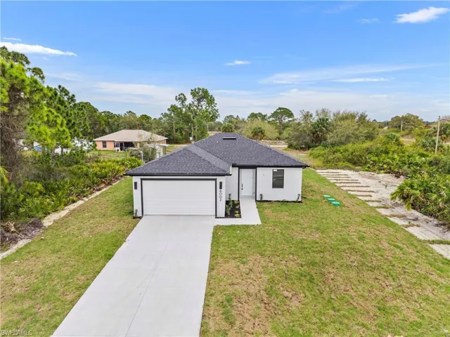 View of front of property featuring a front yard, driveway, a garage, roof with shingles, and stucco siding