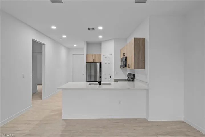 Kitchen featuring a peninsula, light wood-style floors, light stone countertops, black appliances, and modern cabinets