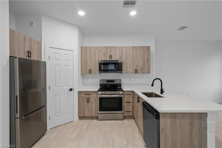 Kitchen featuring a peninsula, stainless steel appliances, light wood finish cabinetry, light wood-style flooring, and light stone counters