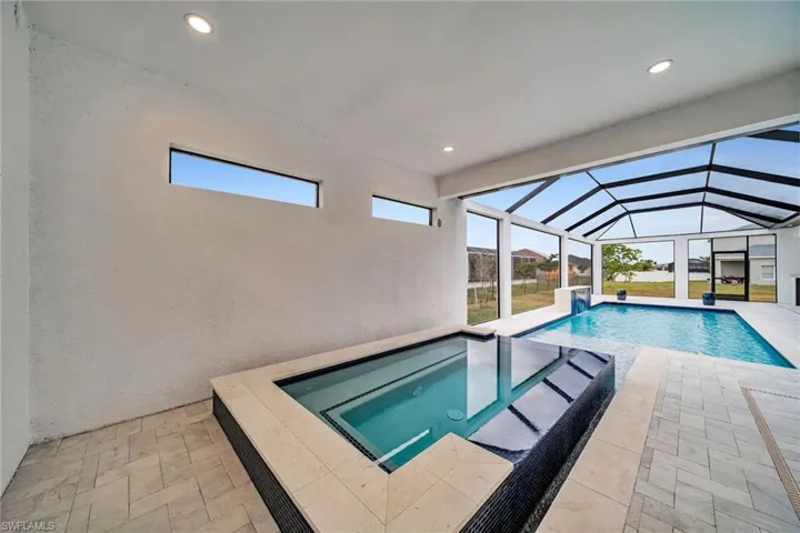 Pool with glass enclosure, a patio, and an in ground hot tub