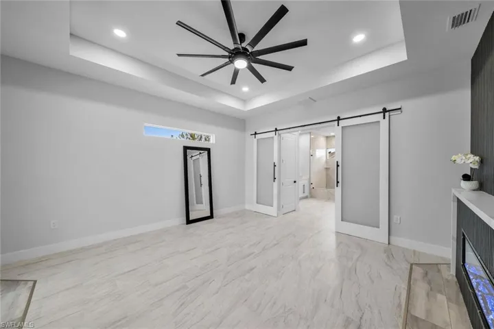 Unfurnished bedroom featuring a barn door, recessed lighting, a tray ceiling, visible vents, and baseboards