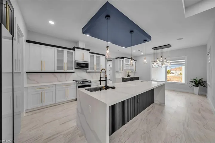 Kitchen featuring white cabinets, a sink, pendant lighting, a kitchen island with sink, and appliances with stainless steel finishes