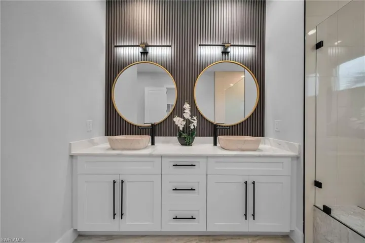 Full bathroom featuring baseboards, double vanity, a stall shower, and a sink