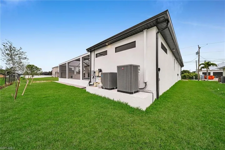 Rear view of property featuring a lawn, central AC, and stucco siding