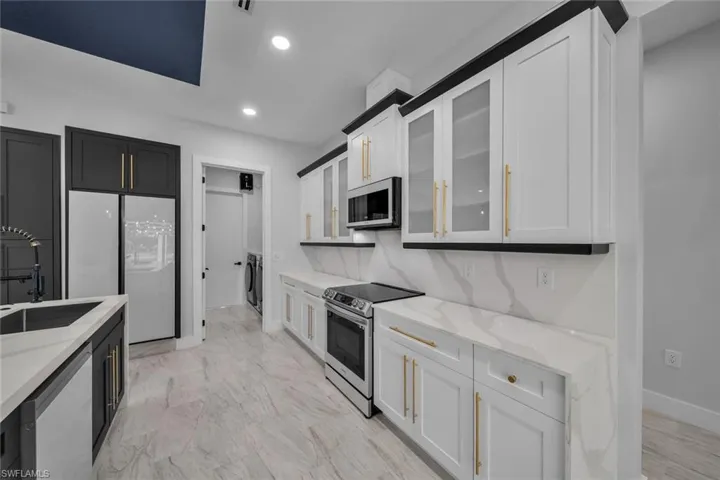 Kitchen featuring light stone counters, a sink, glass insert cabinets, stainless steel appliances, and recessed lighting