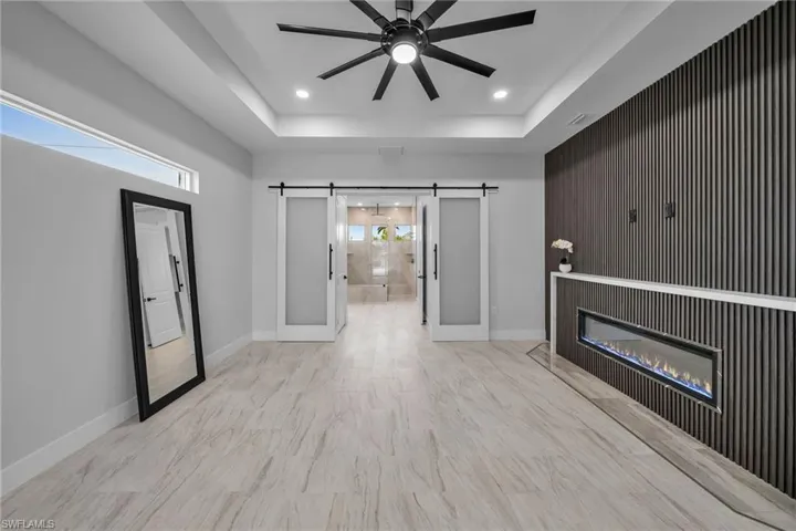 Unfurnished living room with baseboards, a tray ceiling, recessed lighting, and a barn door