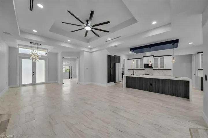 Unfurnished living room with recessed lighting, a raised ceiling, a ceiling fan, a sink, and baseboards