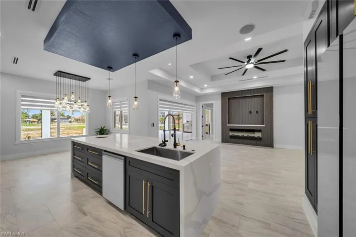 Kitchen with a raised ceiling, dishwasher, a sink, baseboards, and open floor plan