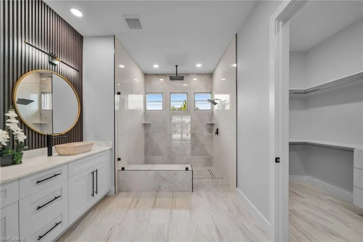 Bathroom with a spacious closet, vanity, marble finish floor, a walk in shower, and visible vents