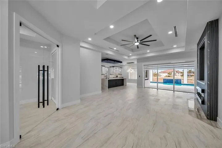 Unfurnished living room featuring ceiling fan, marble finish floor, a raised ceiling, baseboards, and recessed lighting