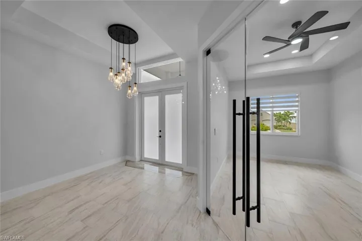 Foyer entrance with ceiling fan with notable chandelier, french doors, a tray ceiling, baseboards, and recessed lighting