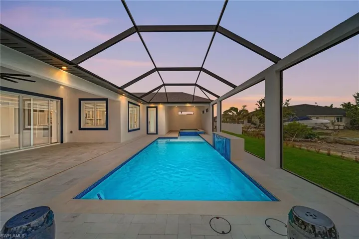 Pool at dusk featuring a yard, a patio area, glass enclosure, and ceiling fan