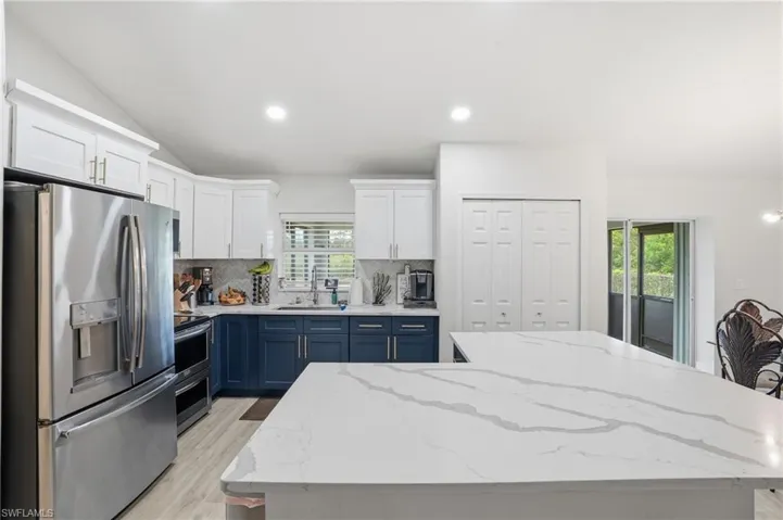 Kitchen featuring two tone cabinetry, stainless steel appliances, light stone counters, a kitchen island, and vaulted ceiling