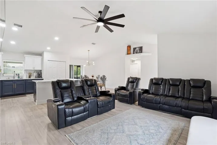 Living area with suspended lighting, a ceiling fan, light wood finished floors, and vaulted ceiling