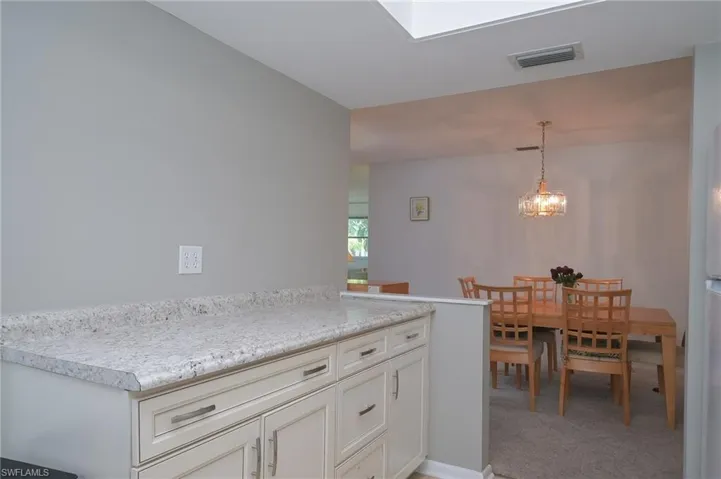 Kitchen with an inviting chandelier, cream cabinets, carpet flooring, and pendant lighting