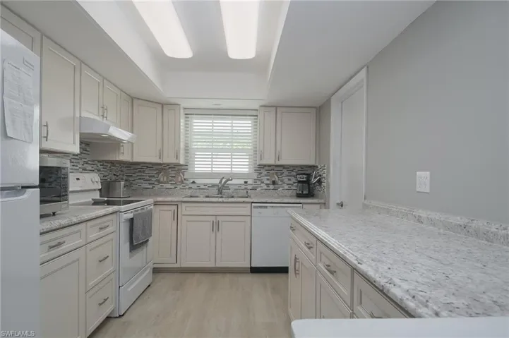 Kitchen with light hardwood / wood-style flooring, white appliances, tasteful backsplash, light  counters, and sink with window Access to the garage off the kitchen.