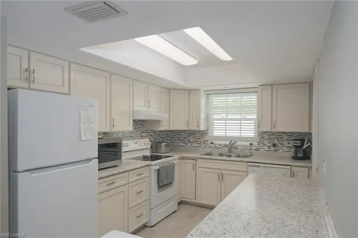 Kitchen with backsplash, sink, light countertops, and white appliances