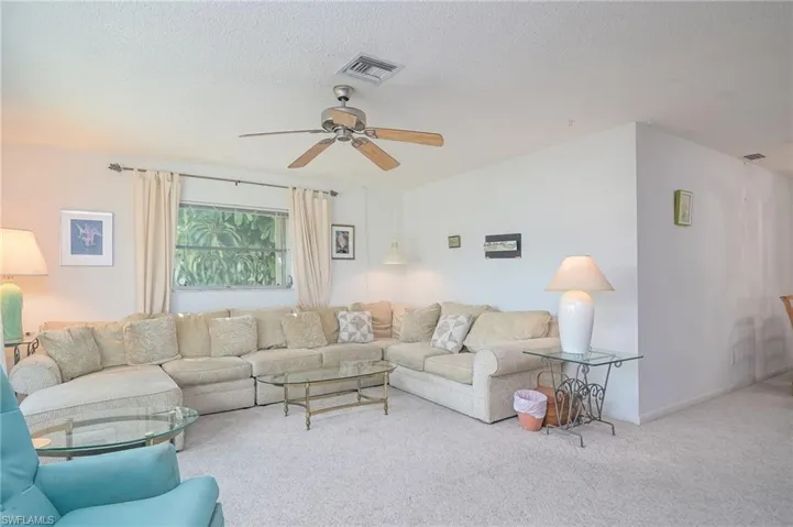Carpeted living room featuring ceiling fan and a textured ceiling
