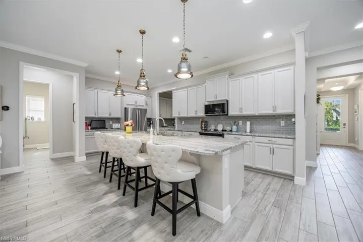 Kitchen featuring a breakfast bar, tasteful backsplash, light stone countertops, white cabinets, and ornamental molding