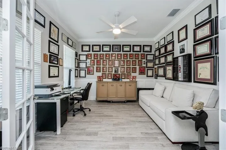 Office space with crown molding, a wainscoted wall, light wood-style floors, a decorative wall, and ceiling fan
