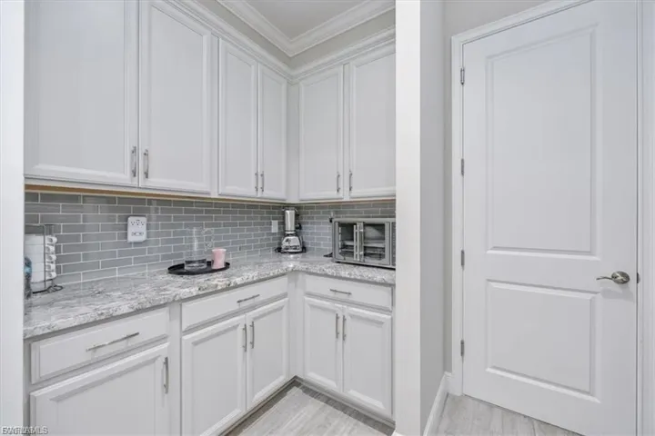 Kitchen featuring white cabinets, ornamental molding, light stone countertops, and decorative backsplash