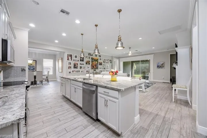 Kitchen with open floor plan, light stone countertops, ornamental molding, white cabinets, and an island with sink