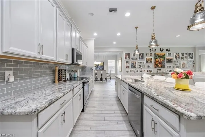 Kitchen featuring pendant lighting, white cabinetry, stainless steel appliances, light stone counters, and ornamental molding