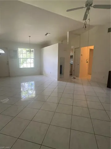 Tile flooring throughout, ample natural light from the window, white walls, and a ceiling fan