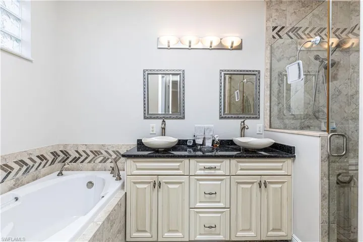 owners suite offers elegant dual sinks with separate tub and shower surrounded by designer tile