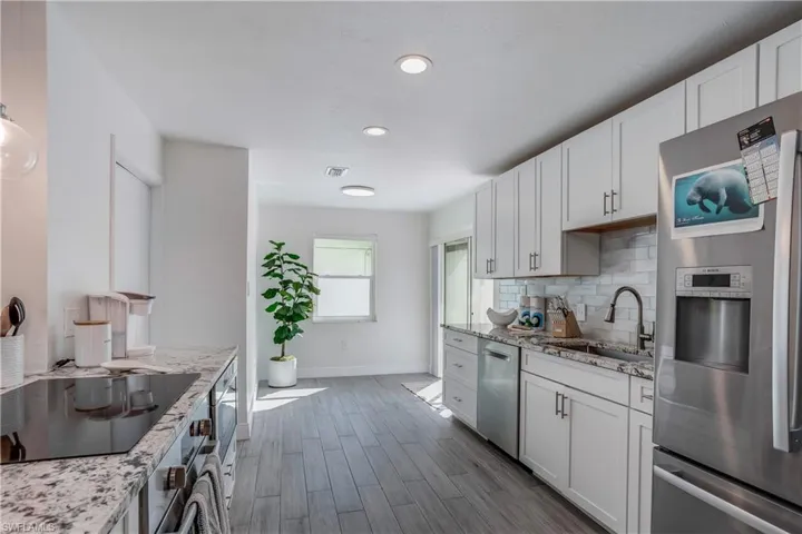 Kitchen with a sink, white cabinets, appliances with stainless steel finishes, light stone countertops, and tasteful backsplash