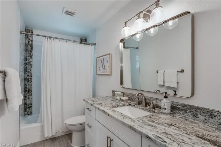 Bathroom with visible vents, toilet, wood finished floors, shower / bath combination with curtain, and vanity