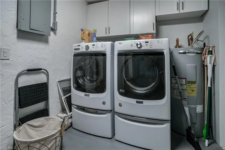 Washroom featuring cabinet space, electric panel, a textured wall, electric water heater, and washing machine and dryer