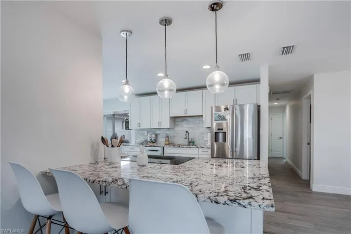 Kitchen with pendant lighting, visible vents, white cabinets, stainless steel fridge, and a peninsula
