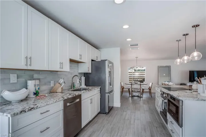Kitchen with appliances with stainless steel finishes, decorative light fixtures, a sink, white cabinetry, and backsplash