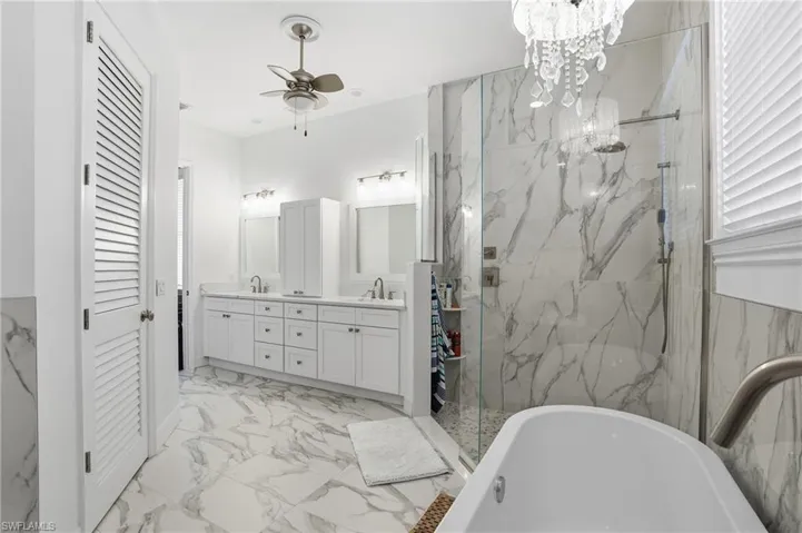 Bathroom with a soaking tub, double vanity, light marble finish flooring, a marble finish shower, and a ceiling fan