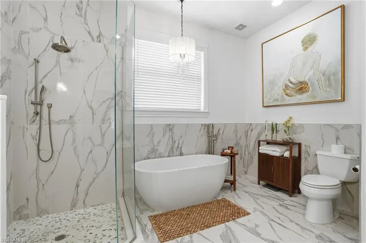 Full bathroom with a marble finish shower, a freestanding tub, tile walls, a wainscoted wall, and recessed lighting