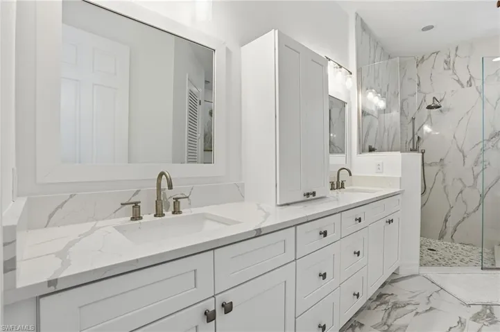 Bathroom with double vanity, a marble finish shower, and light marble finish floors