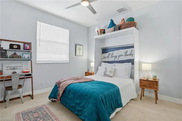 Bedroom with light colored carpet, a ceiling fan, and an office area