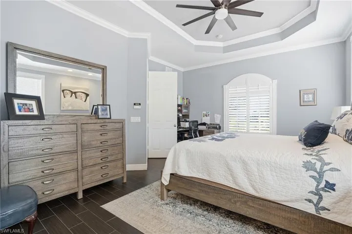 Bedroom featuring wood tiled floors, ceiling fan, ornamental molding, and a raised ceiling