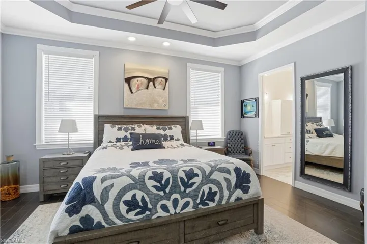 Bedroom with wood finish floors, a raised ceiling, crown molding, connected bathroom, and ceiling fan