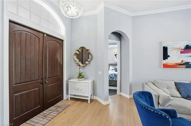 Foyer entrance with crown molding, light wood-style floors, arched walkways, and a chandelier