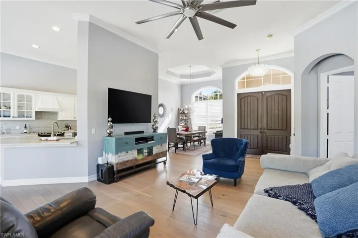 Living room with light wood finished floors, ceiling fan, ornamental molding, and a chandelier